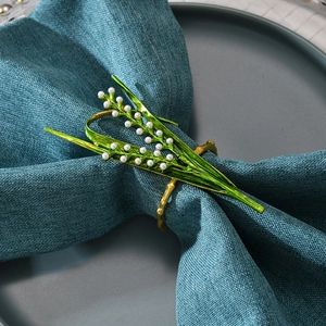 Elegant lily of the valley napkin ring with white pearls and green leaves on a blue napkin