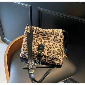 Detail of leopard print crossbody bag with black leather strap and metal buckle accents