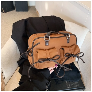 Détail du sac à bandoulière caramel avec poches à nœuds sur un fauteuil beige