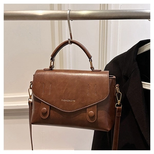 Brown vintage faux leather crossbody bag hanging beside a black suit on a white wall