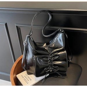Detailansicht der schwarzen Glanz-Hobo-Tasche mit weißen Kontrastnähten und Schleife