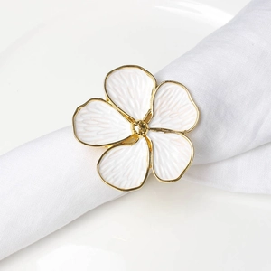 Close-up of golden five-petal flower napkin ring with white enamel petals on white linen