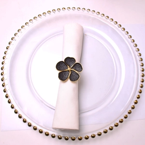 Detail of a black floral napkin ring with gold edges on a white linen napkin