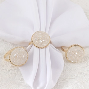 Ronds de serviette dorés avec cristaux blancs sur une nappe en dentelle blanche
