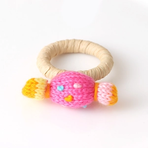 Detail eines handgewebten Serviettenrings aus Stroh mit gestricktem rosa Süßigkeiten-Anhänger