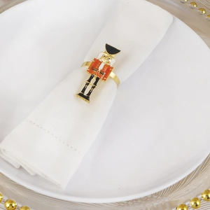 Close-up of golden nutcracker napkin ring on white fabric and gold beaded edge plate