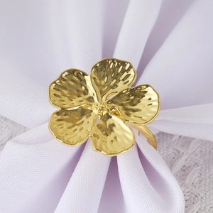 Elegant gold five-petal flower napkin ring with hammered texture on white linen cloth