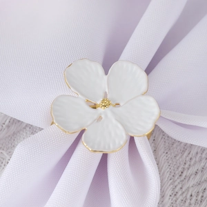 Close-up of white enamel flower napkin ring with gold edges on pleated cloth