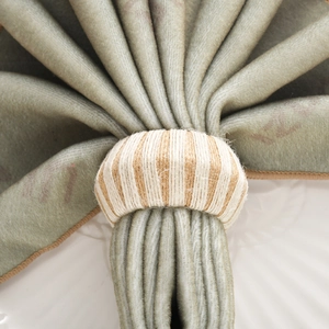 Handmade woven napkin ring with cream and brown stripes on a rustic dining setup