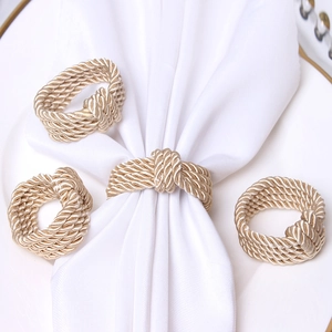 Set of four gold braided rope napkin rings on a white plate with white napkin decor