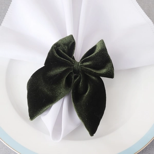 Dark green velvet bow napkin ring set on a blue-rimmed white plate with minimalist decor