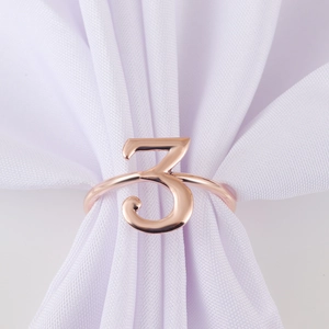 Detailed close-up of rose gold number 3 napkin ring on white fabric background