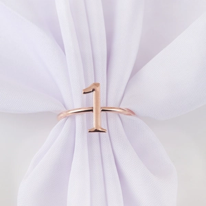 Close-up of number 1 napkin ring in rose gold finish on white silk fabric for events