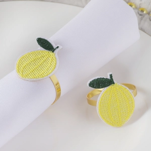 Detail of two handmade lemon embroidered napkin rings with gold metal bands on a white plate