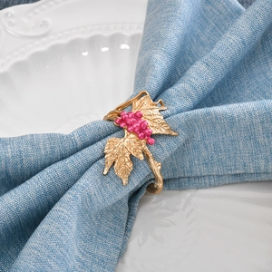Zinc alloy grape napkin ring with pink fruits and gold leaves on a blue linen napkin