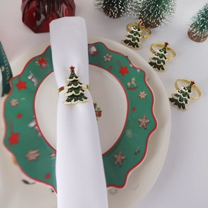 Detailed view of green enamel Christmas tree napkin rings with golden bow on festive table