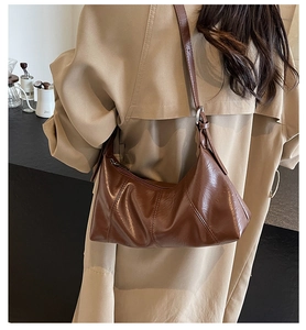Close-up of brown glossy hobo bag with adjustable strap and silver buckle on a trench coat