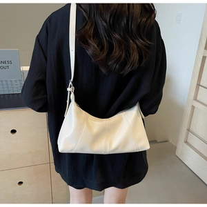 Minimalist beige crescent bag in oily leather texture shown worn by a model from behind