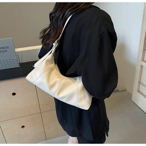 Model wearing a cream wax leather crescent shoulder bag with minimalist interior styling