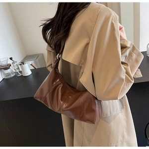 Detail of dark brown vintage crescent bag with pleats and stitching on a beige trench coat