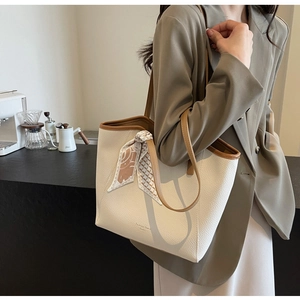 Detail of beige faux leather tote with brown trim and decorative scarf near coffee machine