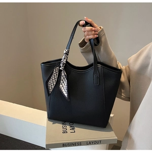 Detail of black pebbled leather tote bag with elegant geometric silk scarf on handle