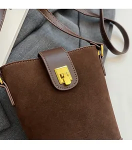 Detail of brown suede crossbody bucket bag with elegant golden rectangular metal lock