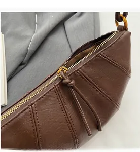 Détail de la fermeture éclair dorée et coutures sur le sac croissant en cuir marron foncé