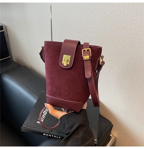 Close-up of burgundy bucket bag with suede texture and gold metal lock detail