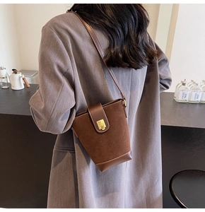 Detail of dark brown bucket bag with metal lock buckle and adjustable shoulder strap