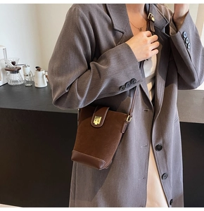 Detail of dark brown suede bucket bag with gold clasp shown on a crossbody model