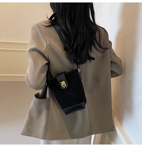 Medium black bucket bag with gold square buckle worn by a model in a beige suit