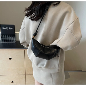 Détail du sac croissant noir avec bandoulière nouée et finition lisse brillante