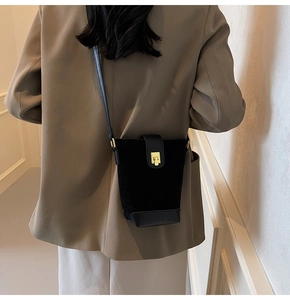Detailed view of a black suede bucket bag with leather trim and gold buckle on a model