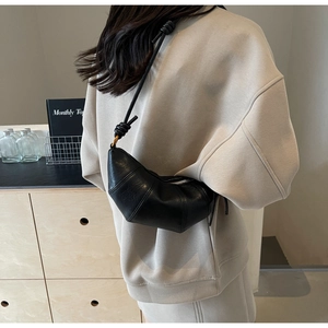 Détail du sac croissant noir avec panneaux en cuir cousus et bandoulière à nœuds