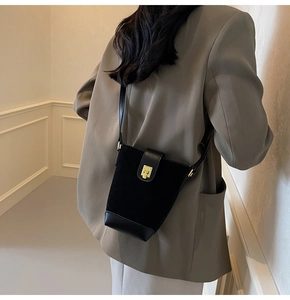 Detail of a black minimalist bucket bag with a gold square lock on a gray blazer