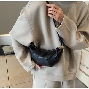 Détail du sac croissant en cuir noir avec bandoulière nouée sur un pull beige