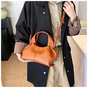 Close-up of caramel leather handbag showing premium lychee texture and side pleats