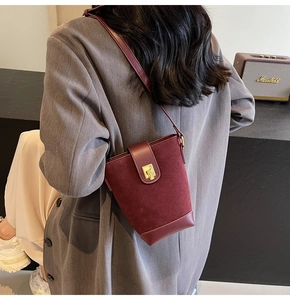 Detail view of burgundy bucket bag with suede texture and golden metal twist lock