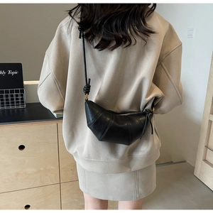 Détail d'un sac croissant noir en cuir avec bandoulière nouée porté par un mannequin