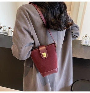 Detailed view of burgundy suede bucket bag with gold buckle on a crossbody shoulder strap