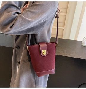 Detail of burgundy suede bucket bag featuring a square gold buckle and leather trim