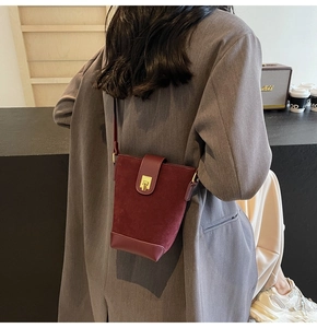 Detail of burgundy suede bucket bag featuring golden twist lock and smooth leather base