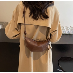 Détail du sac croissant en cuir marron foncé avec bandoulière nouée sur un trench kaki
