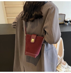 Detail view of burgundy patchwork bucket bag with suede texture and gold clasp on model