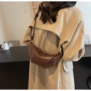 Détail d'un sac croissant marron avec bandoulière à nœud sur un trench-coat beige