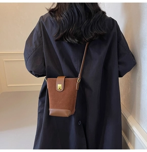 Detail of vintage brown bucket bag with gold metal buckle on a minimalist long coat