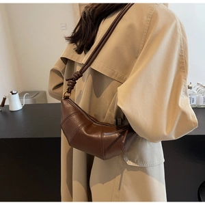 Détail du sac croissant en cuir marron foncé avec bandoulière nouée sur un mannequin en trench
