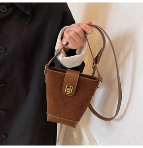 Brown vintage suede bucket bag with gold lock shown held by a woman in a black coat