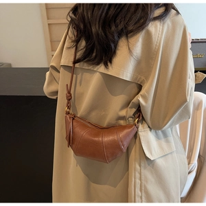 Détail d'un sac croissant en cuir marron montrant les coutures et la bandoulière nouée